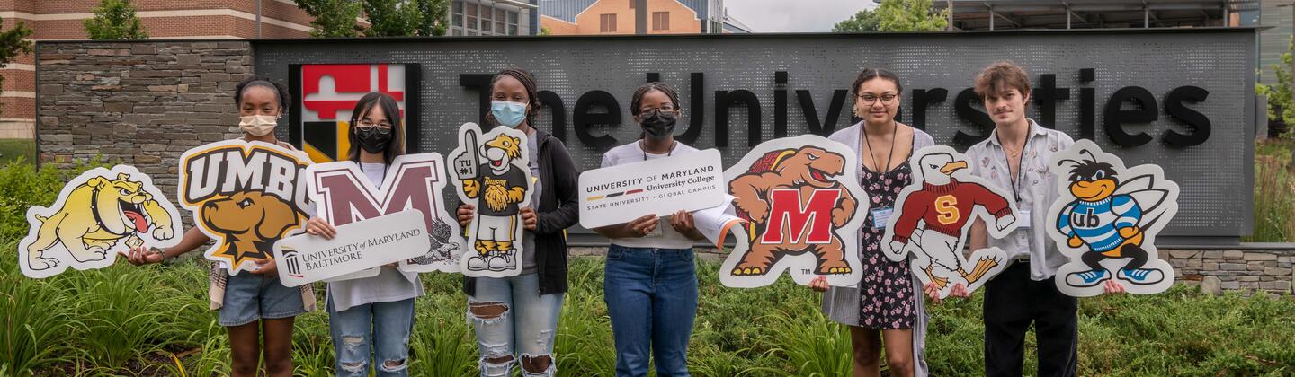 Students posing for a picture holding USG partner institution logos