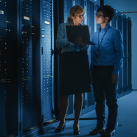 Two people speaking and walking by technology stacks