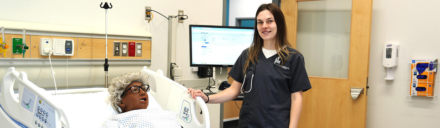 Nursing student, Lexi Vipavetz, in nursing simulation lab with hospital bed and manikin