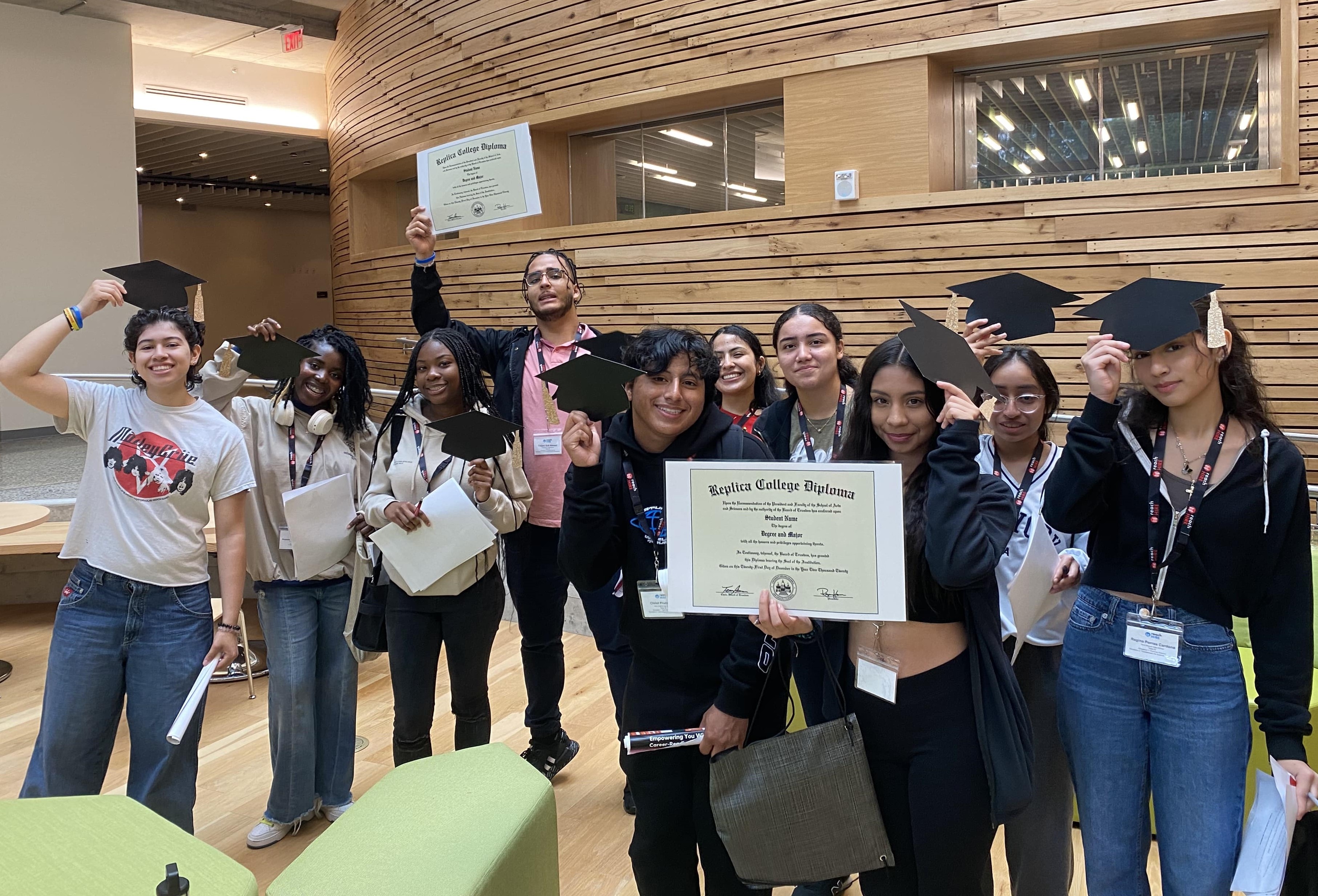Students hold cardboard grad caps and diplomas